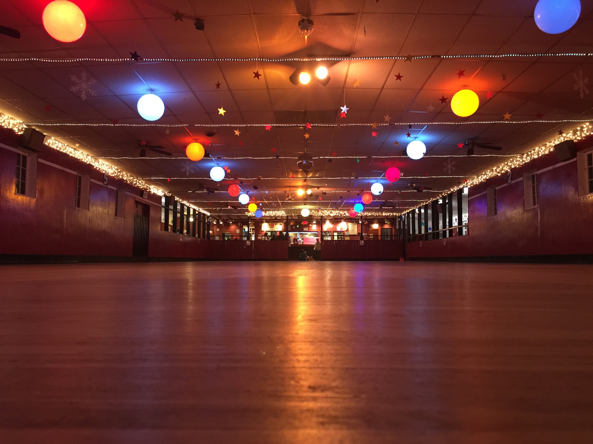 An empty roller rink reflects warm light beneath colorful hanging globes and strings of stars.