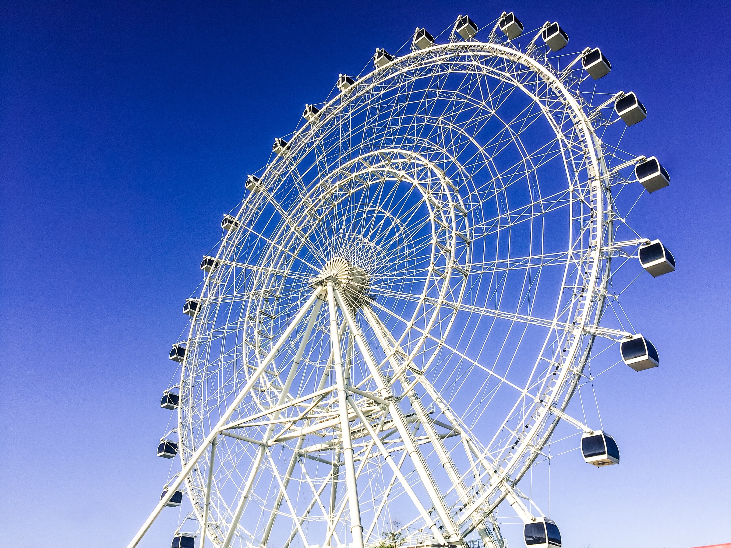 A bright white Ferris wheel photographed from below against an intensely blue sky.